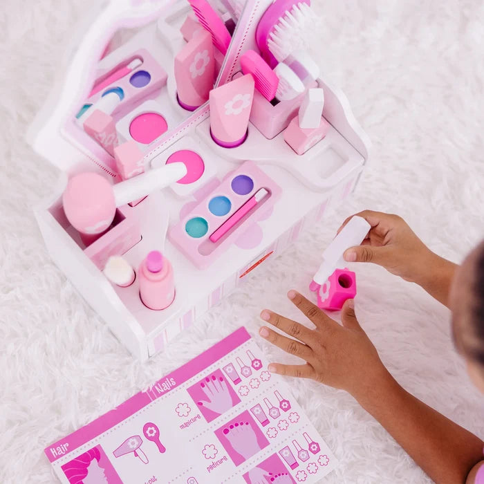 Pink wooden toy vanity set with makeup and hair accessories being used by a child on a white plush rug.