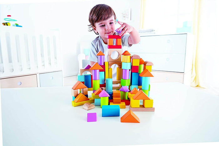 Young child building a tower with multicolored wooden blocks in shapes like cylinders, triangles, and cubes.