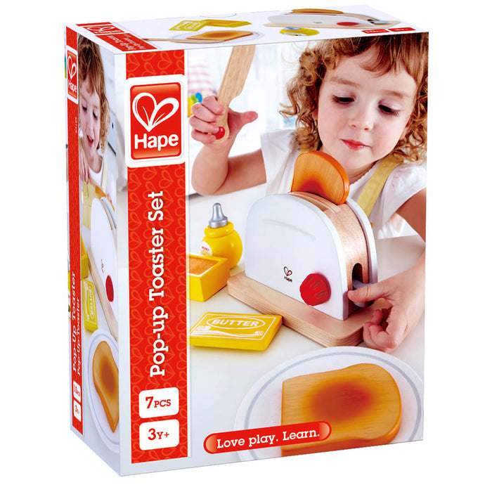 Hape box shows a child playing with a white wooden toaster, red dial, toy bread, butter, honey, and a wooden knife.