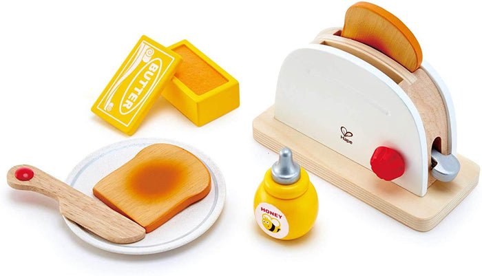 Wooden toy toaster with toast, red knob, yellow honey bottle, butter dish, plate, and spreader on white background.