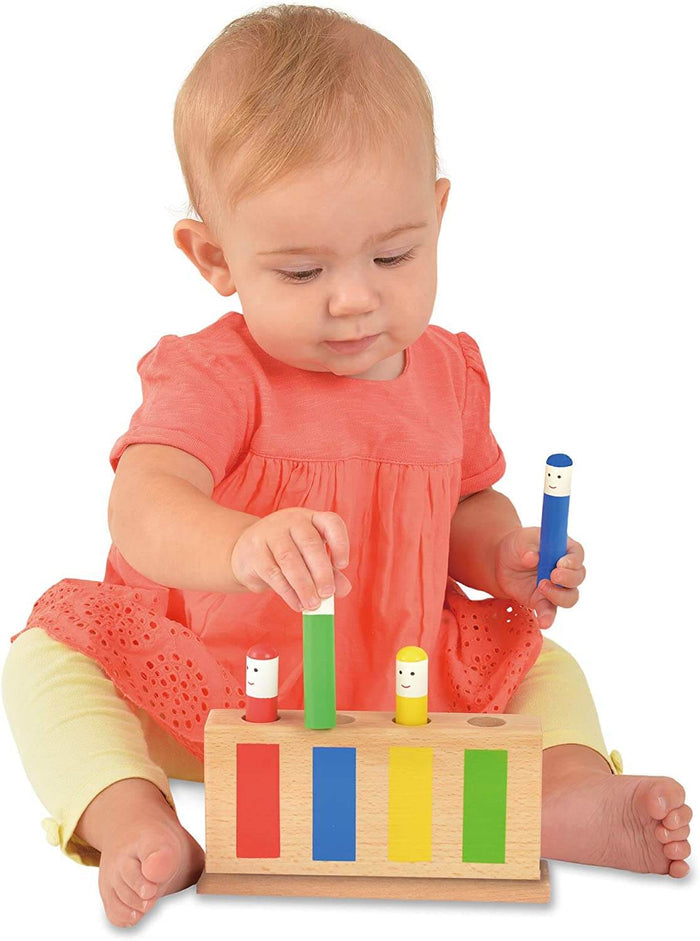 Baby playing with a wooden toy base and four colorful, smiley-faced pegs in red, blue, yellow, and green.