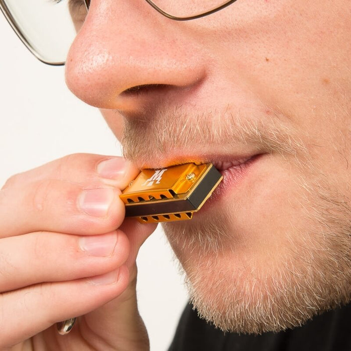 Close-up of a person holding a tiny gold and black harmonica to their lips to show its miniature scale.