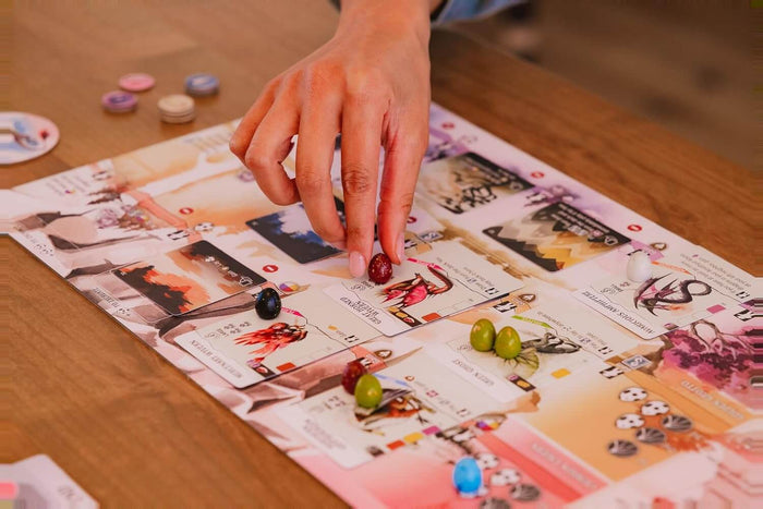 Hand placing a red egg token onto a colorful dragon-themed board game with cards and various small game pieces.