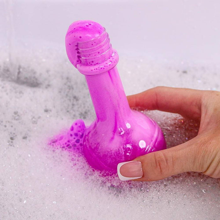 Hand holding a bright purple potion bottle-shaped bath fizzie bubbling and dissolving in soapy water.