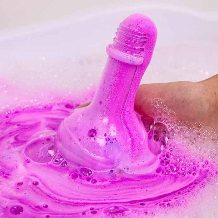 Purple potion-bottle-shaped bath fizzer bubbling with vibrant pink foam in a tub of soapy water.