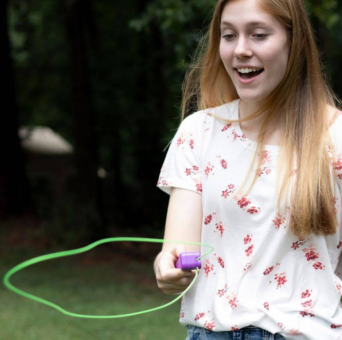 A girl holds a purple handheld device launching a large neon green loop of string that floats in mid-air.
