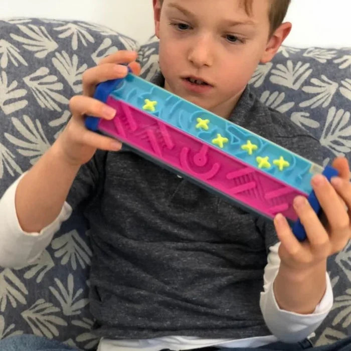 Boy holding a hexagonal maze toy with blue end caps, pink and blue internal pathways, and small yellow obstacles.
