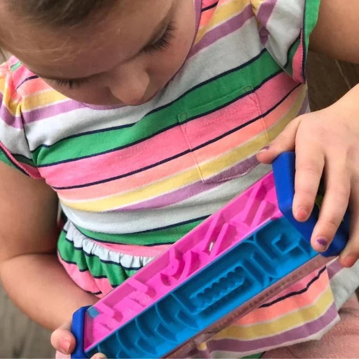 Child holding a clear hexagonal toy with bright pink and blue maze levels and a small silver ball inside.